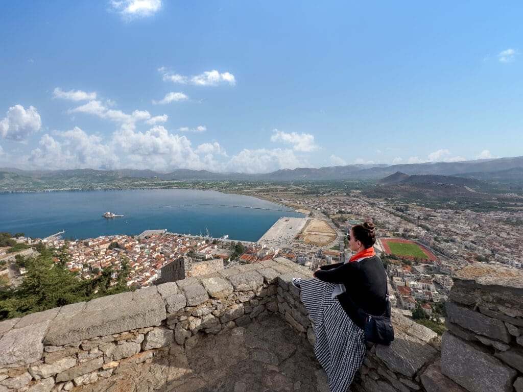 A man sitting on top of a stone wall overlooking the ocean.